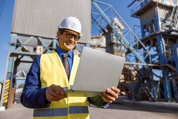 Joyful matured man wearing work vest and safety helmet while holding notebook and smiling