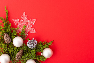 Fototapeta na wymiar A beautiful frame for your New Year and Christmas greetings On a red background, green coniferous branches, Christmas balls, cones and a white openwork snowflake. Postcard, banner, advertisement.