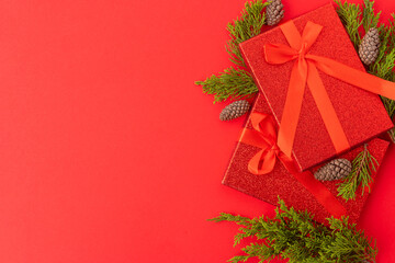 Stylish Christmas and New Year composition on a red background. Beautifully wrapped gifts, pine branches and cones. A beautiful frame for your congratulations.