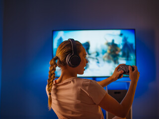 The girl is emotionally playing a video game. Blue neon light. Shooting in profile. Night, insomnia, video games, gambling business, strategy games, hobby, rest, quarantine.
