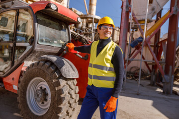 Joyful matured man in work vest and safety helmet looking away and smiling while placing hand on...