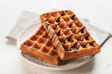 Plate with delicious Belgian waffles and chocolate sauce on light background, closeup