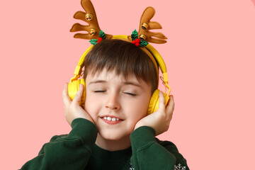 Little boy listening to Christmas music on color background