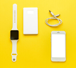 Modern power bank, smartwatch and mobile phone on yellow background