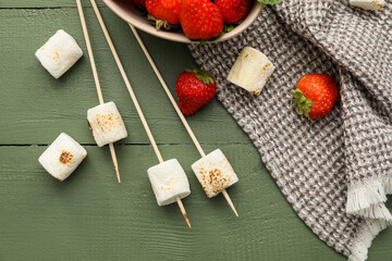 Skewers with tasty grilled marshmallows and strawberry on green wooden background