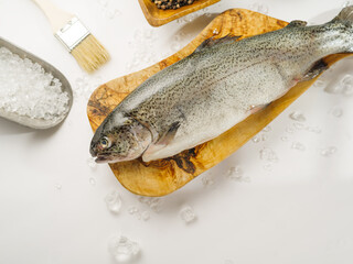 One fresh fish on a cutting board, salt and spices on a white plate. Salting and marinating fish, restaurant, cookbook, culinary blog, advertising. High angle view.