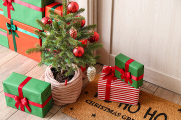 Small Christmas tree with gift boxes near light wooden door