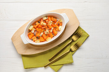 Dish with tasty baked pumpkin pieces on white wooden background