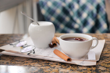 Cup of hot tea, eyeglasses and music notes on table in cafe