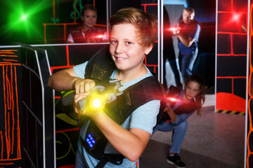 Emotional teen boy with laser pistol playing laser tag with his family on dark room