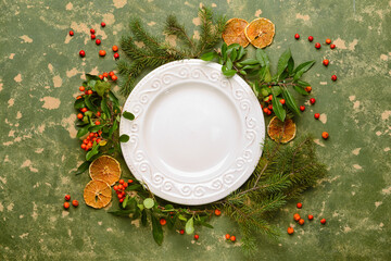 Composition with table setting, fir branches and lingonberries on green background
