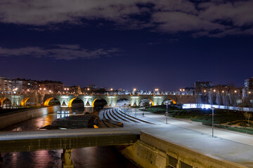 Night view of the Manzanares river in Madrid with the old bridge of Toledo and some modern walkways