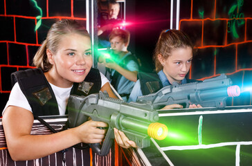 Positive girl with laser gun having fun on laser tag arena with her teen sister