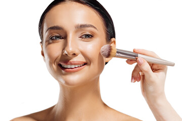 Beautiful young woman applying cosmetic powder to her face with a brush, skin care concept, on a white background