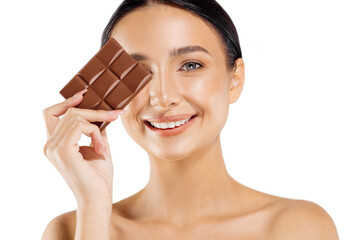 beautiful woman with dark hair, bare shoulders and neck, holding a bar of chocolate to enjoy the...