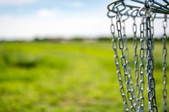 Disc golf goal chains gently swaying in the breeze with a green course in the background