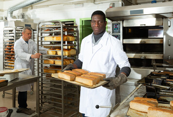 Fototapeta na wymiar African-american baker spreads hot bread on a pallet. High quality photo