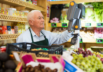 European man greengrocer worker standing at counter and checking cash register.