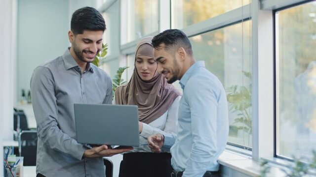 Multiethnic colleagues listens Arabic team leader explain corporate task application to diverse workers indian businesspeople looking on laptop screen working together, teamwork brainstorm concept