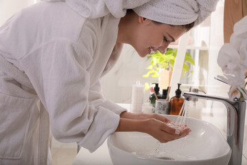 Fototapeta na wymiar Beautiful teenage girl washing face with cleansing foam in bathroom. Skin care cosmetic