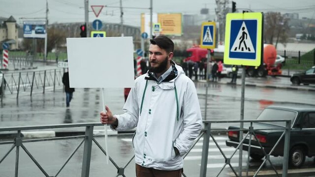 Bearded young adult guy holds white clear card board for advert while marching. People walking with ads blank poster panel for text design. Empty banner sign with motion tracking points in display