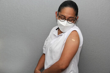 Latin young adult woman with glasses shows her arm recently vaccinated against covid-19 in the new...