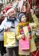 Cheerful preteen girl with father shopping decorations on Christmas market..