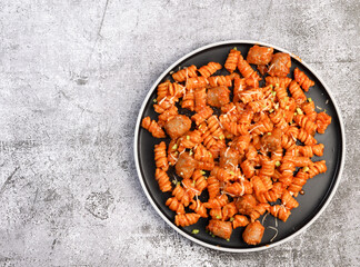 Pasta with sausages and cheese on a round plate on a dark background. Top view, flat lay