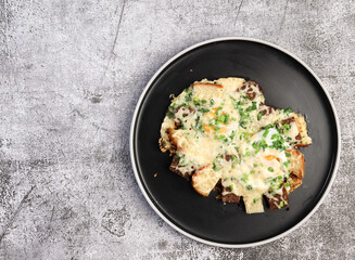 Fried eggs with bread, cheese and green onions on a round plate on a dark background. Top view, flat lay