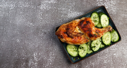 Roasted chicken on a rectangular plate on a dark background. Top view, flat lay