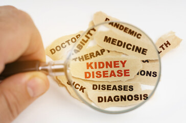 A man looks through a magnifying glass at a piece of paper, in the center of which is the red inscription KIDNEY DISEASE