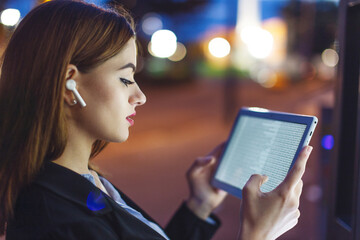 Young businesswoman with hands free device working on tablet at night in city