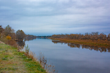 Two banks of the same river on a cloudy day. Autumn landscape of the river and yellowed forest.
