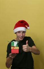 A teenage boy in a Santa hat with gift boxes makes a thumb gesture.