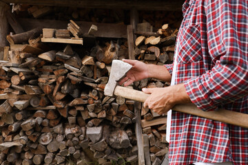 Man with sharp ax near wood pile outdoors, closeup