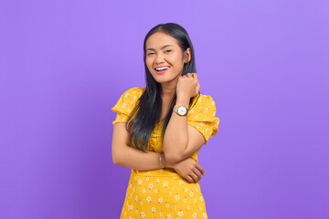 Portrait of smiling young Asian woman raised hand with a crossed arm on purple background