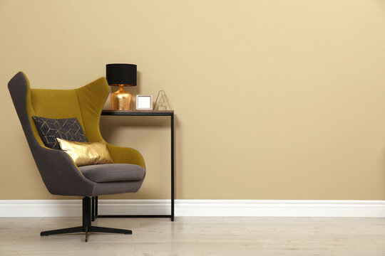 Armchair and console table near beige wall in room, space for text. Interior design