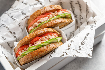two delicious tuna sandwiches with tomato and cucumber in a white box in paper