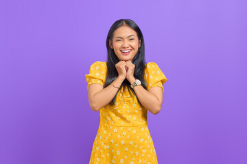 Smiling young Asian woman keeps hand under chin isolated over purple background