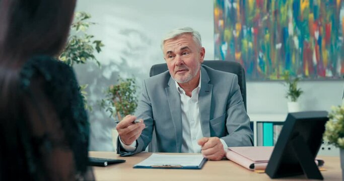Job interview elderly boss with gray hair sitting at desk opposite him woman applying for secretarial position in company man asks girl questions discusses education salary expectations first contract