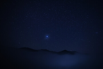 Fototapeta na wymiar Beautiful view of misty mountains under starry sky at night