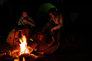 Couple sitting near bonfire in camp at night