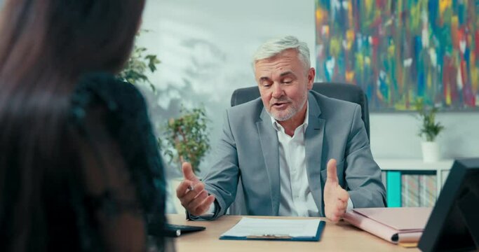 Job interview elderly boss with gray hair sitting at desk opposite him woman applying for secretarial position in company man asks girl questions discusses education salary expectations first contract