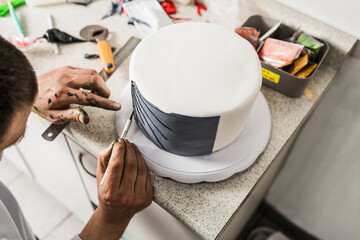 Chef decorating a cake using a awl in a kitchen