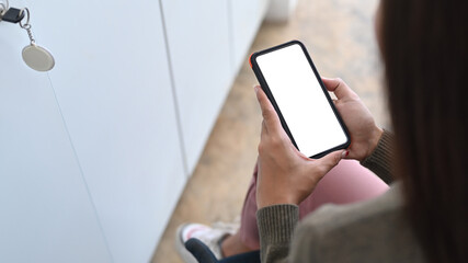 Over shoulder view of young female sitting in office and using smart phone.