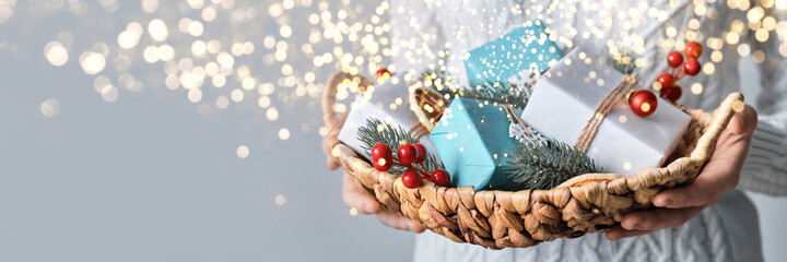 Woman holding basket with sustainable wrapped Christmas gifts, close-up, selective focus. Eco...
