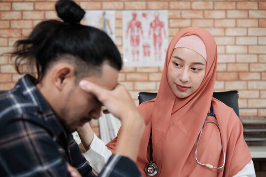 A Young Beautiful Doctor, A Person Who Is Female Muslim Encourages And Comforting Male Patient Of Asian Ethnicity Who Is Sad And Illness, At Health And Medical Treatment Clinic's Office In Hospital.