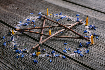 Branch Pentagram - witchcraft tools of natural wood. Wooden pentagram with candles, small stones and blue petals. Occultism and mysticism