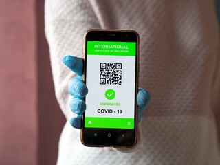 Close up view of woman's hand in glove holding smartphone display in app, mobile vaccinated...