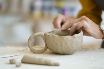 Handcraft therapy at ceramics lesson: close up shot of female hands shaping potter cup. Artist work with raw clay on master class in studio. Practicing handmade hobbies. Develop art skills and talent